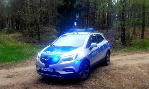 policyjny radiowóz z włączonymi sygnałami świetlnymi stoi na leśnej drodze